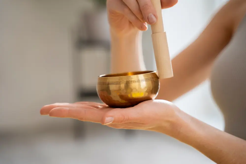 Person holding a small, polished brass singing bowl in the palm of their left hand.