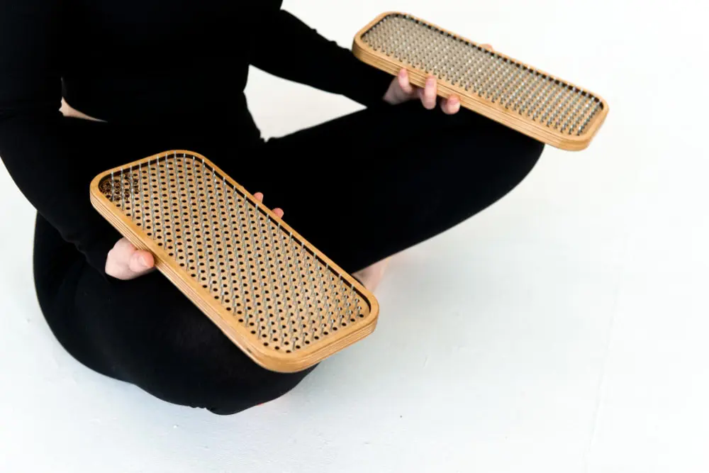 A person holding two rectangular wooden foot massage boards with metal spikes.