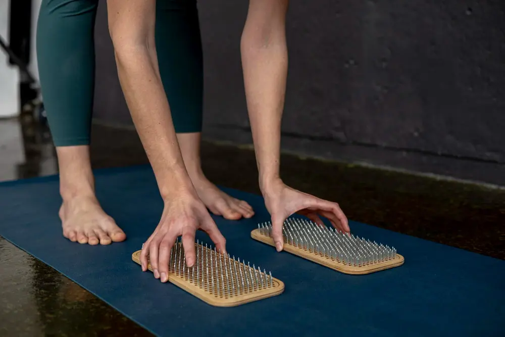 A person placing two wooden foot massage boards with metal spikes on the mat.