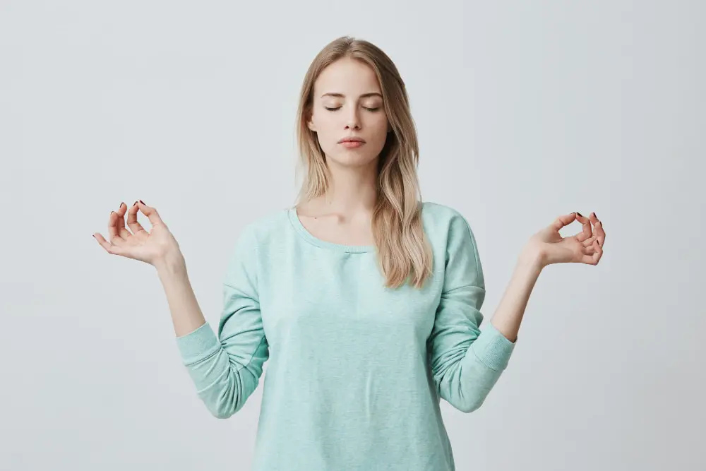 A woman stands with her eyes closed, practicing meditation.