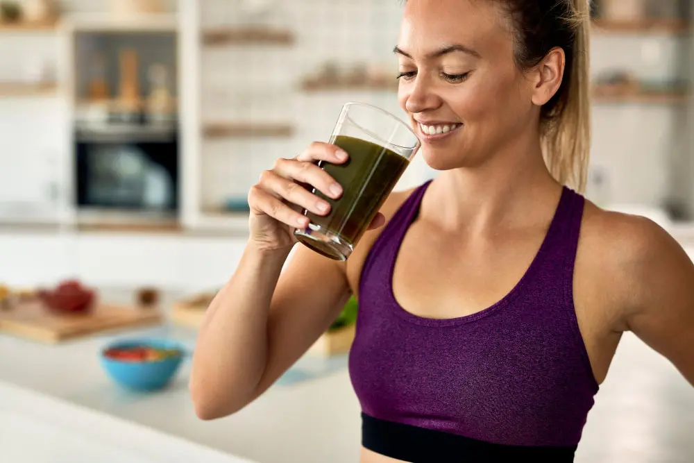 A woman in workout attire enjoys a green smoothie, likely part of her healthy detox retreat routine.