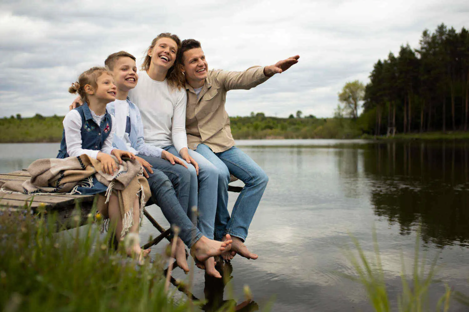 Family sitting on dock by lake, smiling and enjoying the view