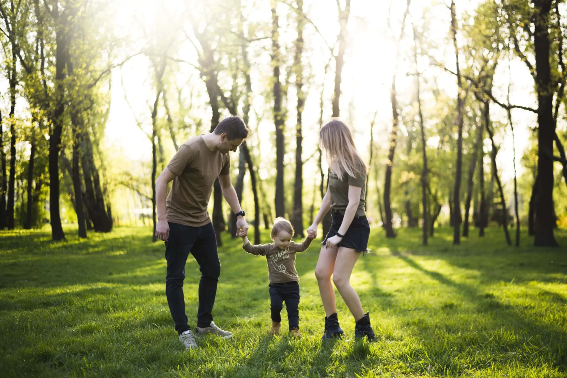 Happy parents holding hands with their child in nature, walking on grass