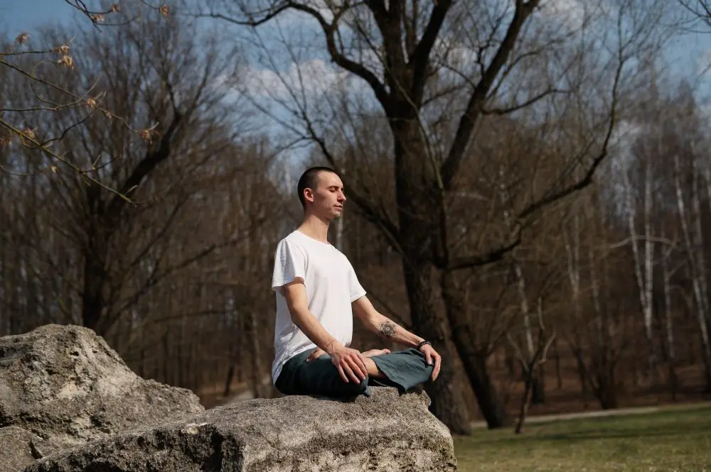 Man meditating in a seated position on a large rock outdoors