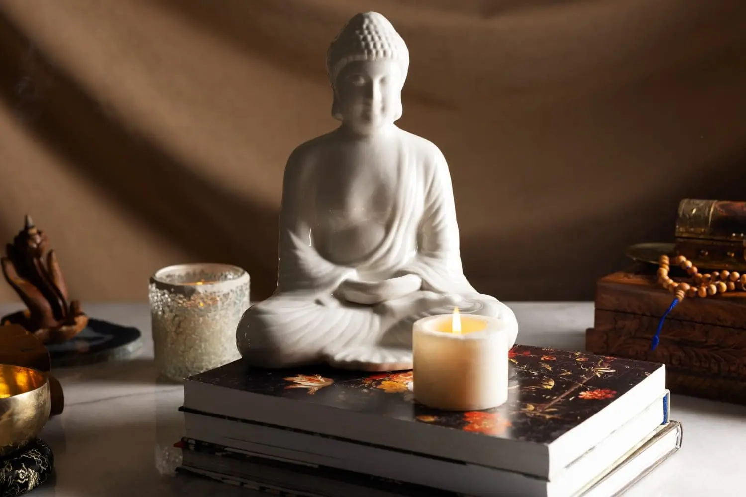 White Buddha statue with lit candle and books on meditation altar