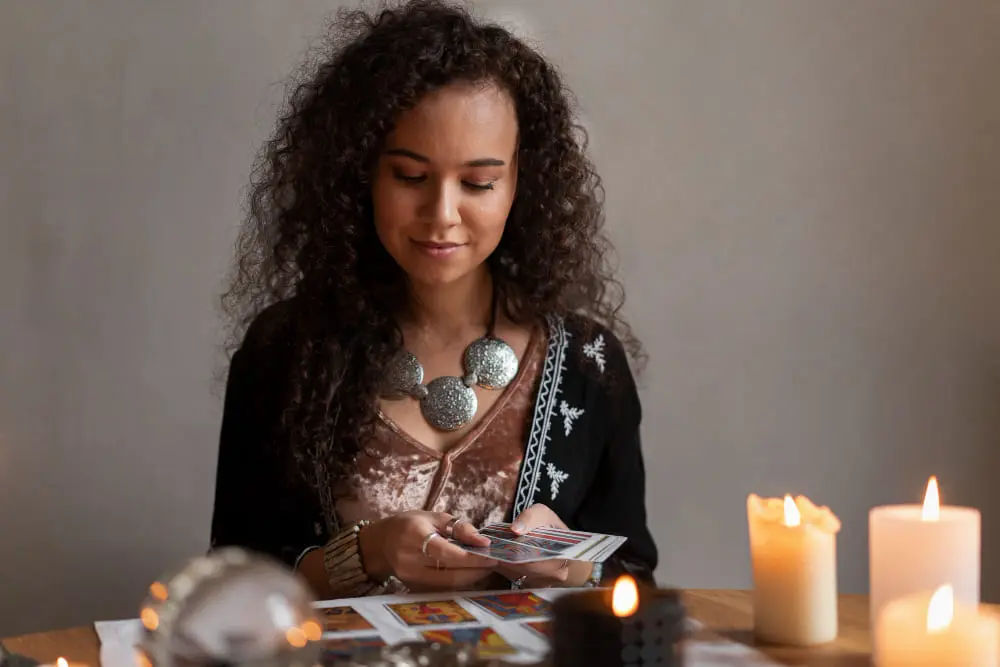 Woman with curly hair reading tarot cards at a table lit by warm candles